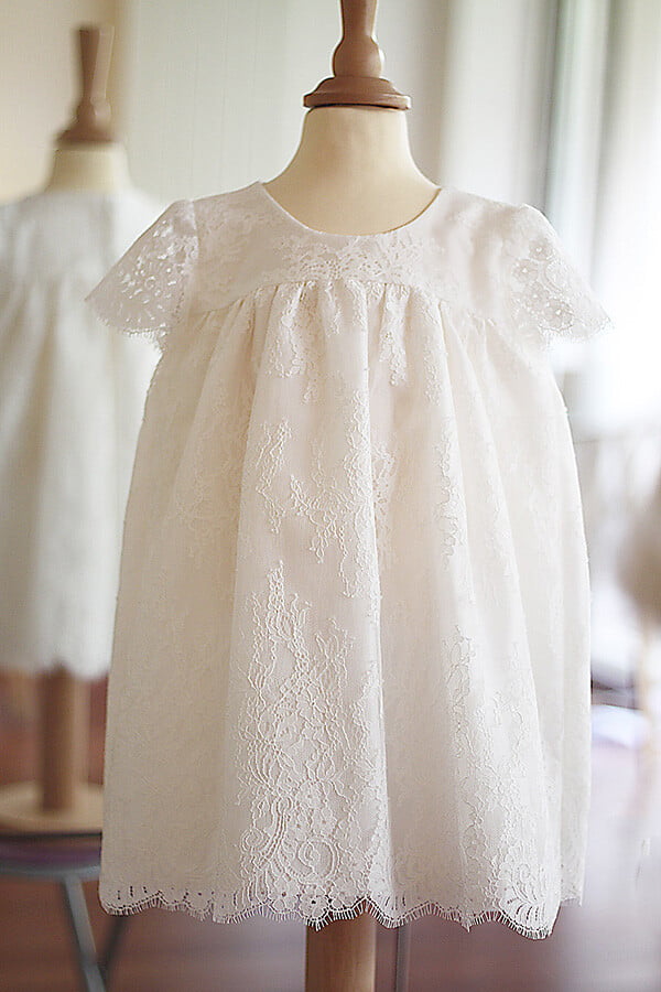 Robe de baptême ou de cérémonie pour bébé et petite fille en dentelle italienne, doublée de coton, modèle été à manches courtes. Création Fil de Légende, disponible en ligne et en boutique à Paris–Neuilly-sur-Seine.